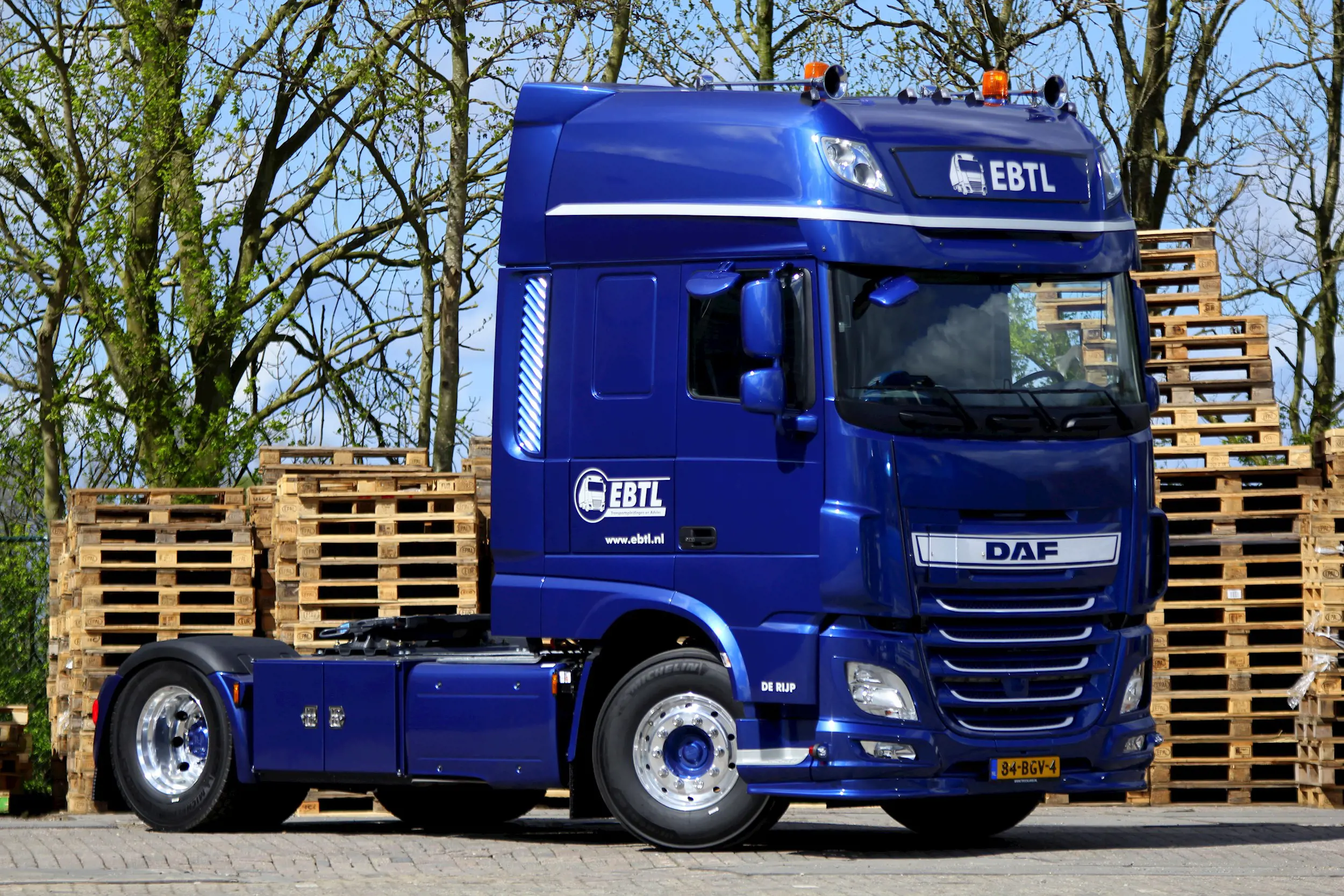 Blauwe EBTL DAF vrachtwagen geparkeerd bij stapels houten pallets op bedrijfsterrein