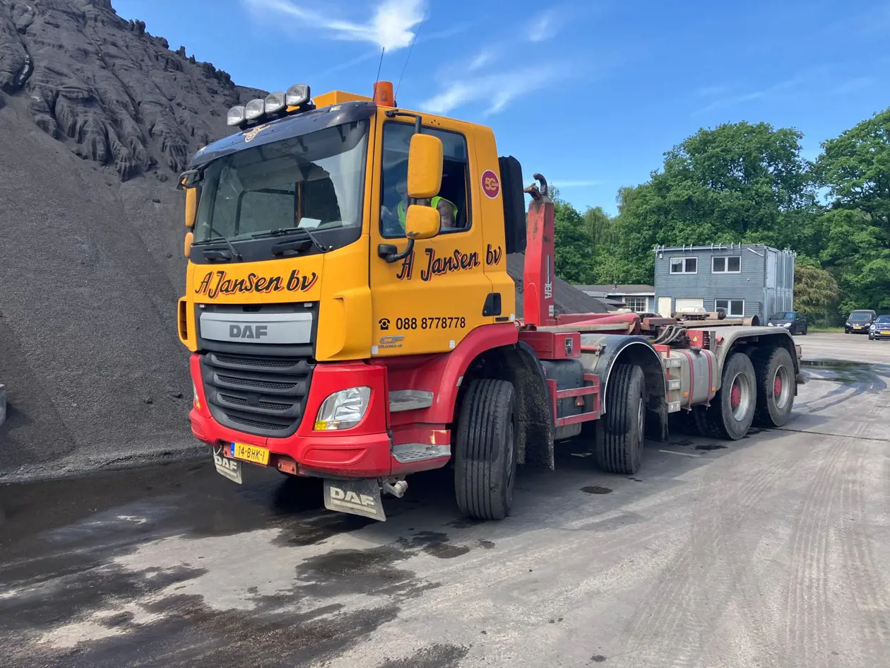 Vrachtwagen met haakarm systeem voor het transporteren en wisselen van containers op bedrijfsterrein