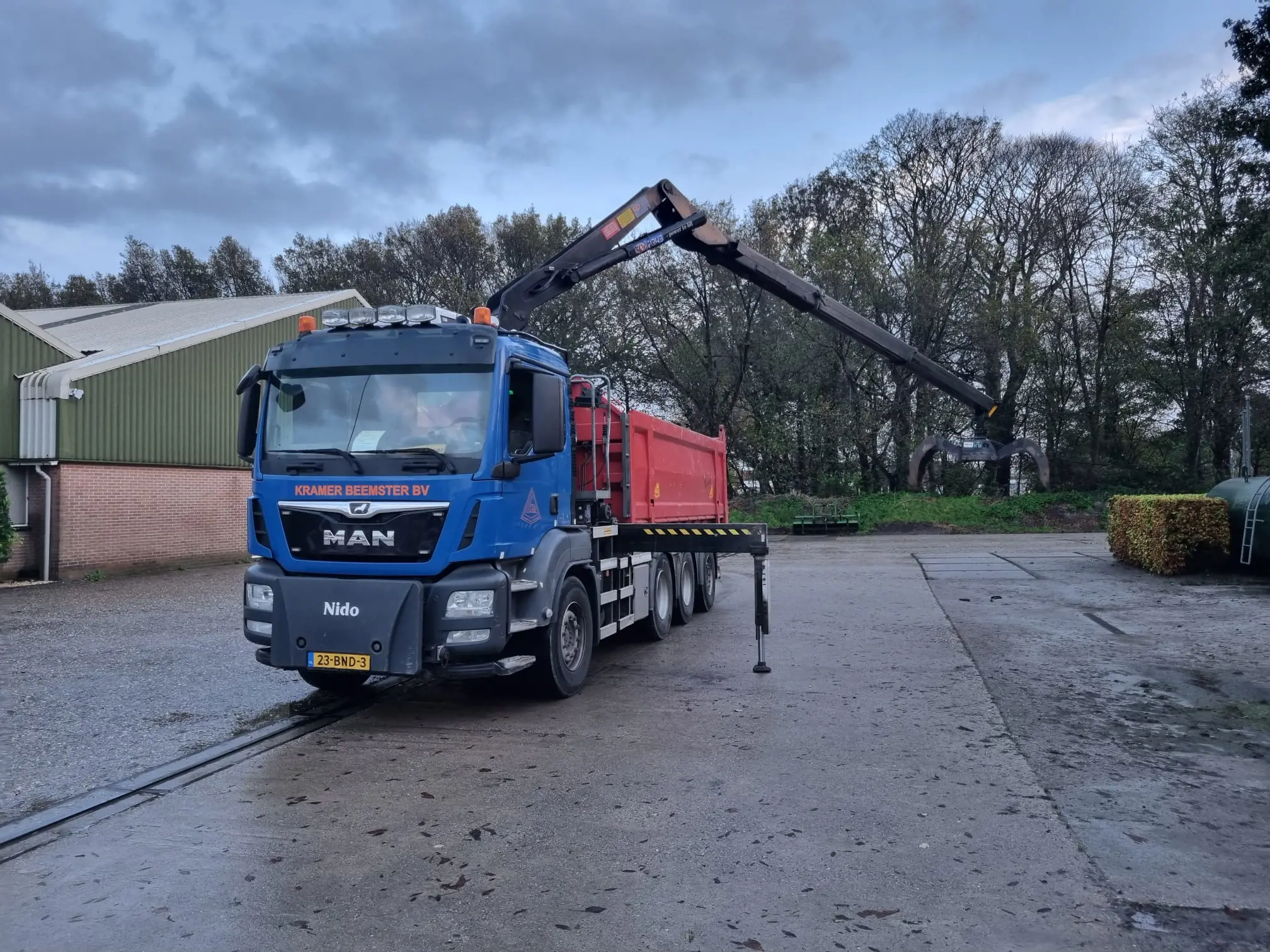 Vrachtwagen met hydraulische laadkraan op bedrijfsterrein voor laden en lossen van materialen