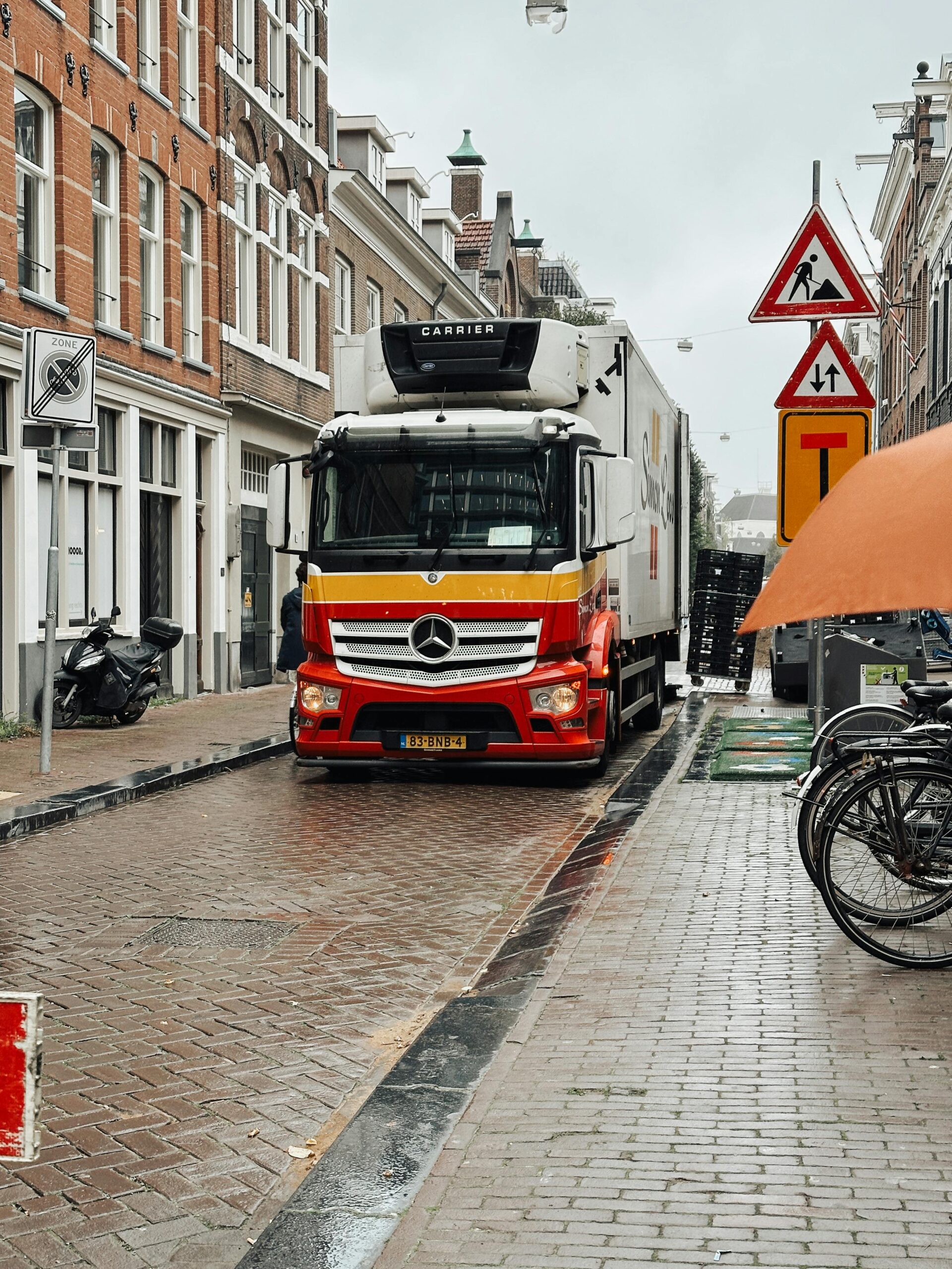Vrachtwagen rijdt door smalle straat in Nederlandse binnenstad met verkeersborden voor milieuzone en wegwerkzaamheden