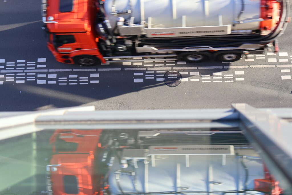 Rode vrachtwagen rijdt over rijbaan in stedelijk gebied gezien van bovenaf met wegmarkeringen op het asfalt