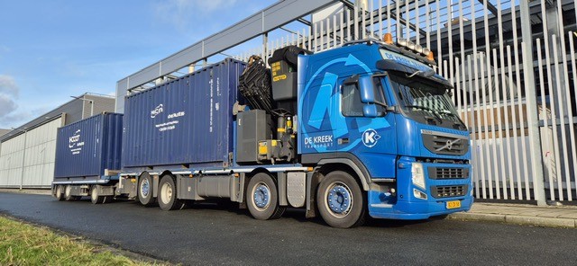 Zware vrachtwagen met dubbel gestuurde vooras en containertransport op oplegger bij bedrijfsterrein